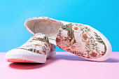 Pair of female's new stylish slip-ons with floral ornament on a pink-blue background. Close up