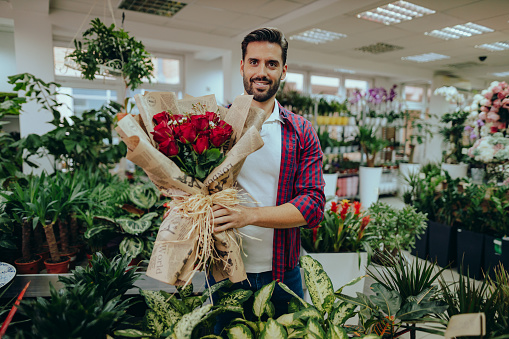 Young male florist holding a red roses flower bouquet in a flower shop