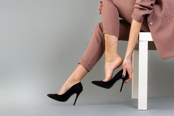 The concept of varicose disease. A woman in a suit takes off her high-heeled shoes. Vascular asterisks are visible on the leg. Legs close up. Gray background The concept of varicose disease. A woman in a suit takes off her high-heeled shoes. Vascular asterisks are visible on the leg. Legs close up. Gray background. dress shoe stock pictures, royalty-free photos & images
