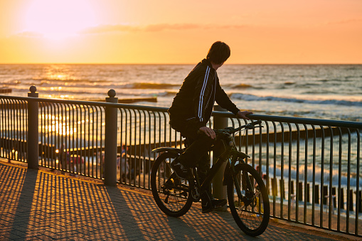 Svetlogorsk, Russia - 08.15.2021 - Cyclist standing and looking at beautiful sunset over blue sea, sport biking on sea coast. Men bicyclist on epic yellow sunset over sea, summer bicycle sport