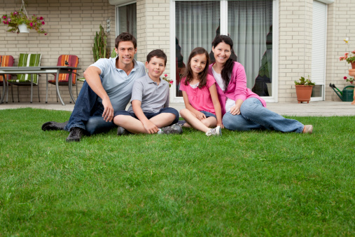 Caucasian family portrait sitting in front of their house smiling