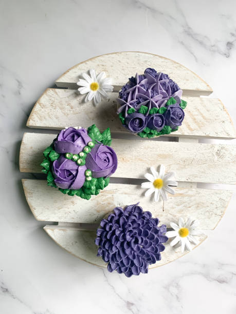 Top view of purple cupcakes decorated with floral theme on white blurry background with some shadow.