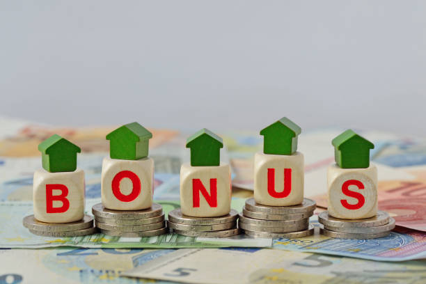 Wooden house and blocks with the word Bonus on coins and banknotes - Concept of home renovation bonus stock photo