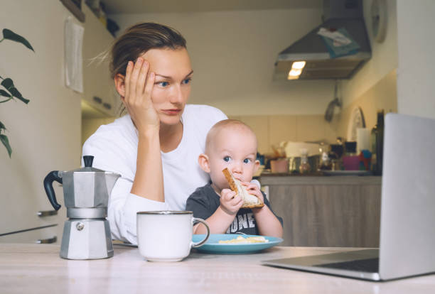 istock Young mother with coffee fighting tiredness while breakfast with baby in kitchen. Freelancer mom and child after sleepless night. Woman studying or working online at home on maternity leave 1370508893