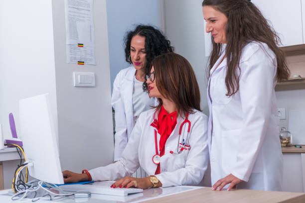 istock ( Medical Team ) Female doctor ( medic ) in her 30's working on her computer while two female nurses stand next to her and discuss a patients illness. 1370509536