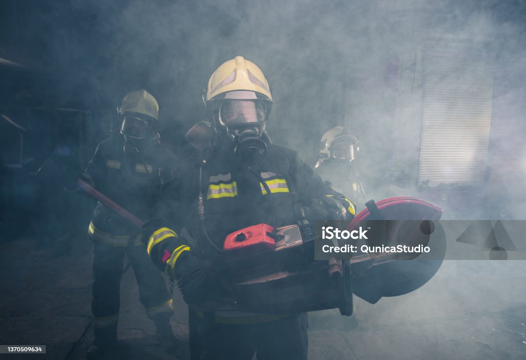 Portrait of fireman holding a rescue chainsaw in smoky garage of the fire department Females Stock Photo