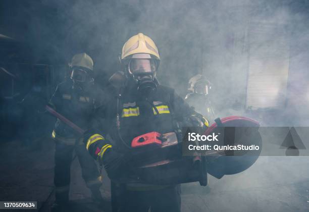 Portrait Of Fireman Holding A Rescue Chainsaw In Smoky Garage Of The Fire Department Stock Photo - Download Image Now