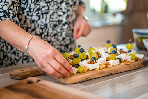Close-up image of hands of an unrecognizable woman prepairing cheese, nuts, grape and blueberries on a wooden cutting board.