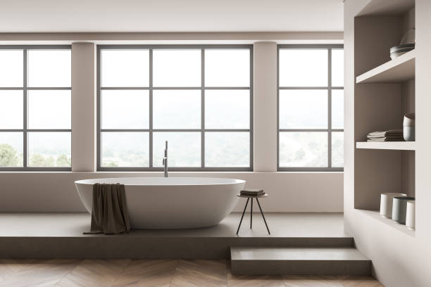 istock Light bathroom interior with bathtub on concrete podium, shelf and window 1370510805