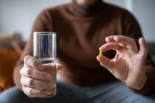 Unrecognisable man holding medicine capsule pill and a glass of water.