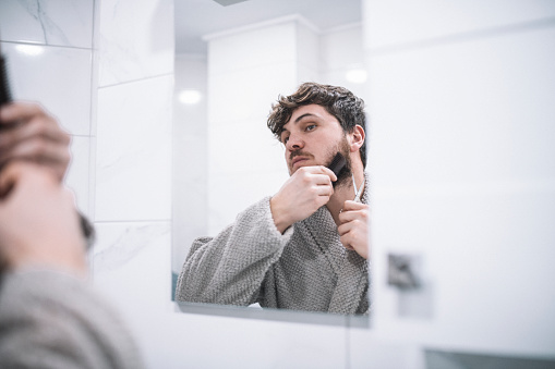 Young man trimming his beard in front of a mirror.