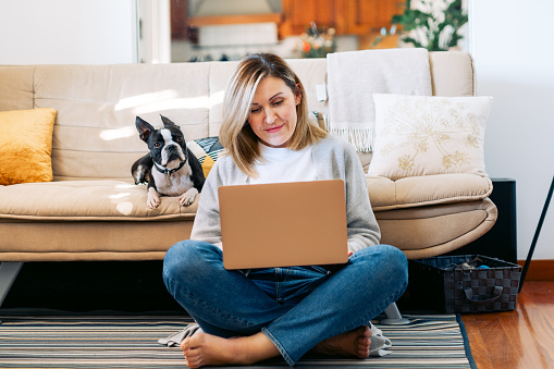 Young woman working from home with a boston terrier dog. Freelancer businesswoman using laptop at sunny room.  Student learning and working at home.