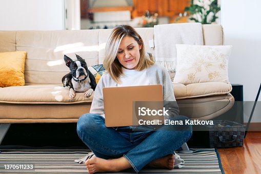 istock Young woman working from home with a boston terrier dog. Freelancer businesswoman using laptop at sunny room.  Student learning and working at home. 1370511233