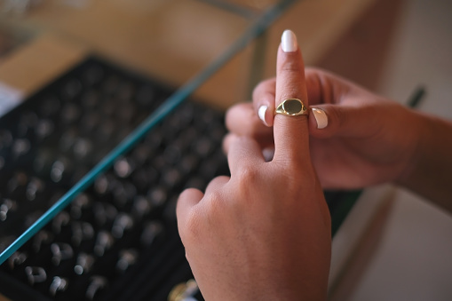 Close-up shot of an unrecognizable female hands with a white manicure trying on a gold index finger at a jewelry store.