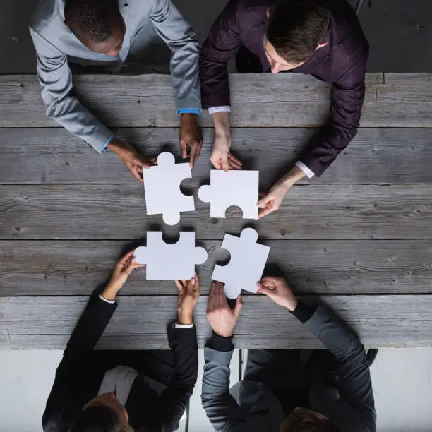 Diverse team people assembling jigsaw puzzle, multiracial group of black and white colleagues engaging in successful teamwork finding business solution, corporate unity teambuilding concept, top view