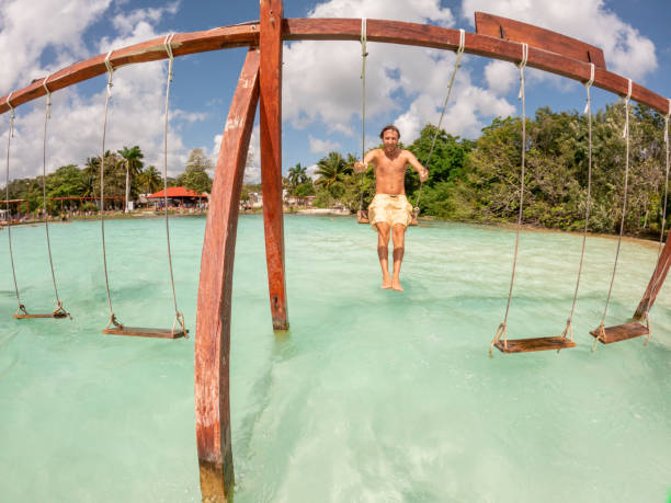 istock Young man having fun on swing in a beautiful lagoon on a sunny day 1370512626