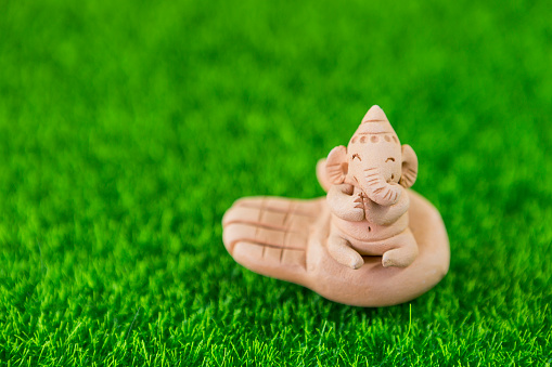 Little Ganesha on hand on green grass background, elephant clay sculpture, garden decoration