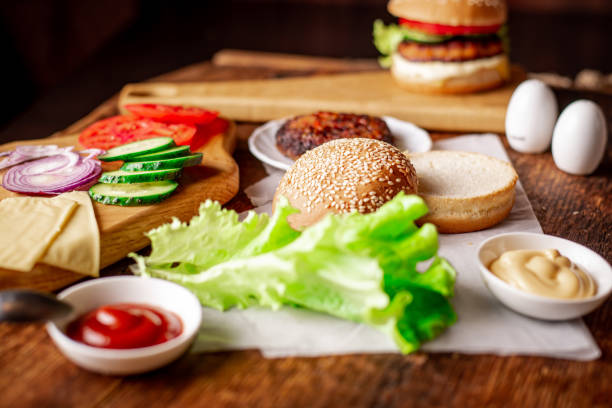 istock Cooking hamburger or cheeseburger. Different ingredients for a classic hamburger. Grilled meat, vegetables, greens, sauces near a sesame bun. Wooden background. 1370516489