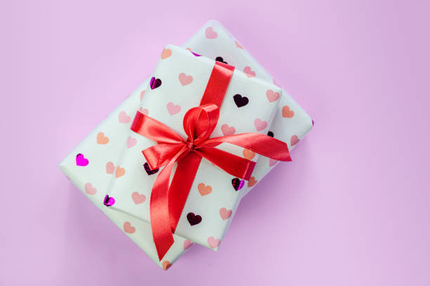 istock Gift boxes wrapped in heart pattern paper with red ribbon bow on pink background 1370517163