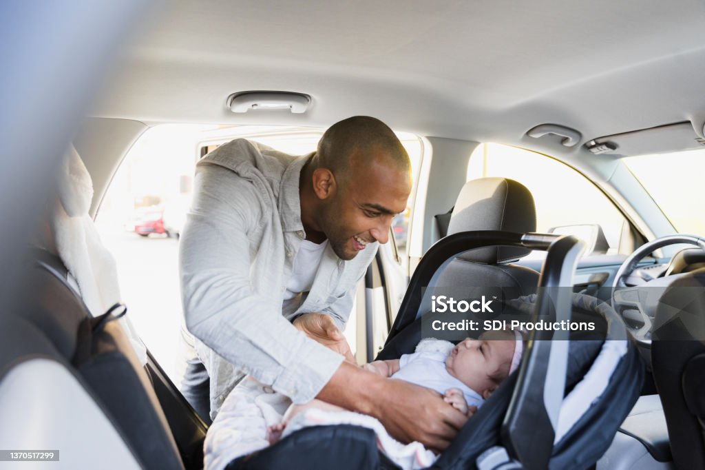 New dad puts baby girl in safety seat in car The new mid adult dad leans into the back of the car as he gently puts his baby daughter in her safety seat. Car Safety Seat Stock Photo