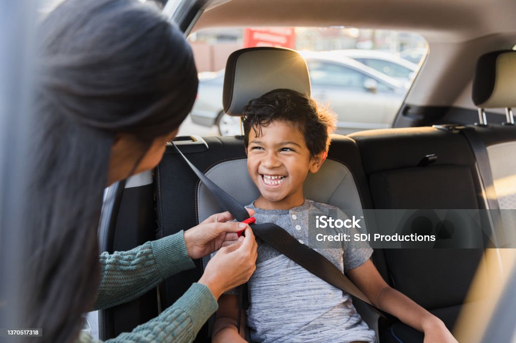 Unrecognizable mother adjusts seat belt for young son The unrecognizable mother adjusts the buckle on the seat belt for her smiling, happy elementary age son. Car Safety Seat Stock Photo