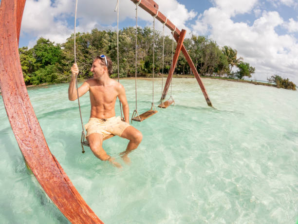 istock Young man having fun on swing in a beautiful lagoon on a sunny day 1370518928