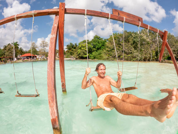 istock Young man having fun on swing in a beautiful lagoon on a sunny day 1370519253