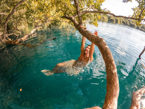 istock Man hangs on a tree in a tropical cenote enjoying nature to the fullest 1370522836