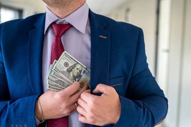 istock Man in blue suit and red tie putting bribe dollar bills into his pocket 1370522853