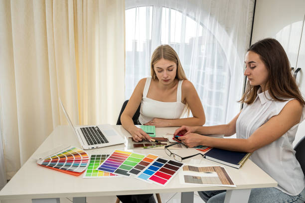 istock two  perfect female workers in white blouses work at a spacious table on a new room design. 1370523108