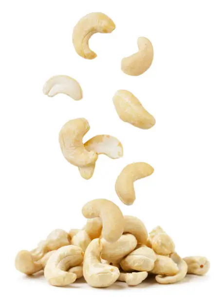 Cashew nuts are falling on a pile close-up on a white background. Isolated