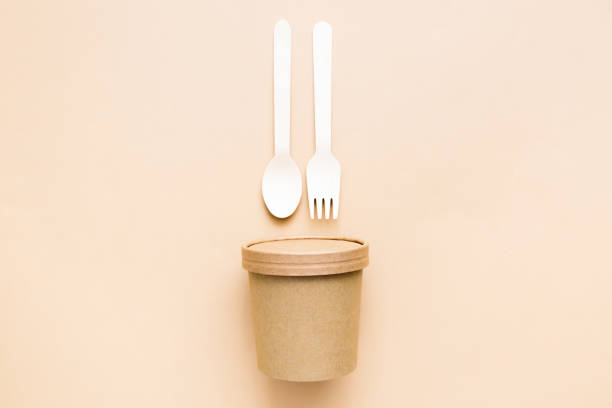 istock Disposable paper cup with wooden fork and spoon isolated on beige background. Eco friendly disposable tableware from natural material. Minimal concept. 1370523317
