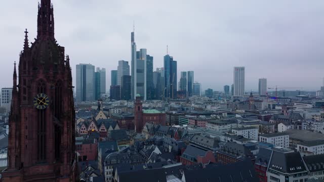 Forwards fly above buildings in urban borough around tower of Frankfurter Dom. Modern office towers in business centre in background. Frankfurt am Main, Germany