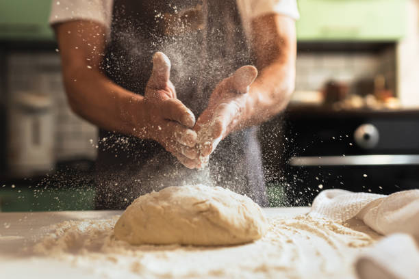 die hände des küchenchefs sprühen mehl über den teig - konditor stock-fotos und bilder