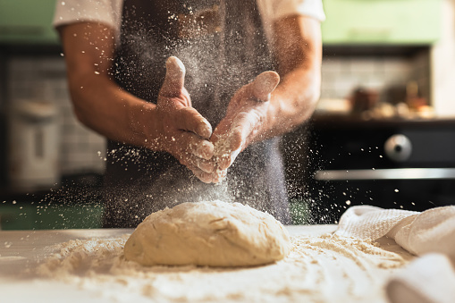 Kneading dough. Male chef in kitchen chef's apron spraying flour over dough