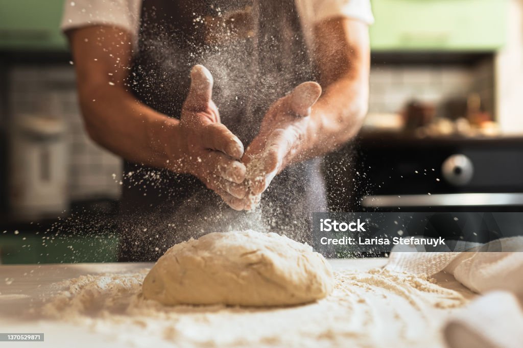 Chef's hands spraying flour over the dough Kneading dough. Male chef in kitchen chef's apron spraying flour over dough Bakery Stock Photo