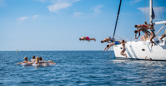 Young people jumping inside ocean in summer excursion day. Happy friends diving from sailing boat into the sea. Vacation, youth and fun concept.