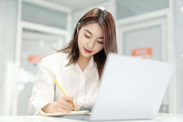 Bored young Asian business woman working with a laptop in the white room. Cheerful and confident Japanese white-collar women stock photo