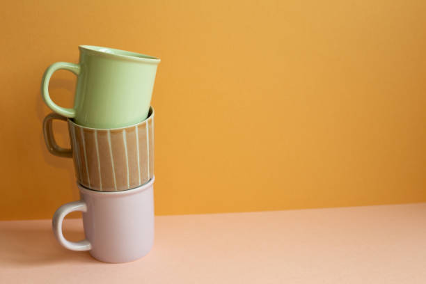 istock Stack of pastel color mug cup on pink table. orange wall background. copy space 1370531885