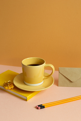 Yellow diary notebook, cup of coffee, pencil on pink desk. orange wall background. copy space