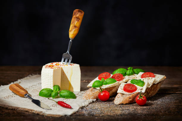Baguette with cherry tomatoes, soft sheeps cheese and basil on a black background. Traditional italian appetizer or snack. stock photo