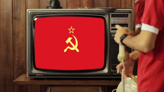 Young Man Talking on Old Phone and Flag of the Soviet Union on Old TV.