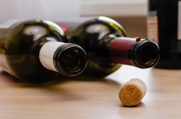duas garrafas vazias de vinho e uma rolha estão aleatoriamente sobre a mesa. o conceito do problema do abuso de álcool. - abuso de álcool - fotografias e filmes do acervo