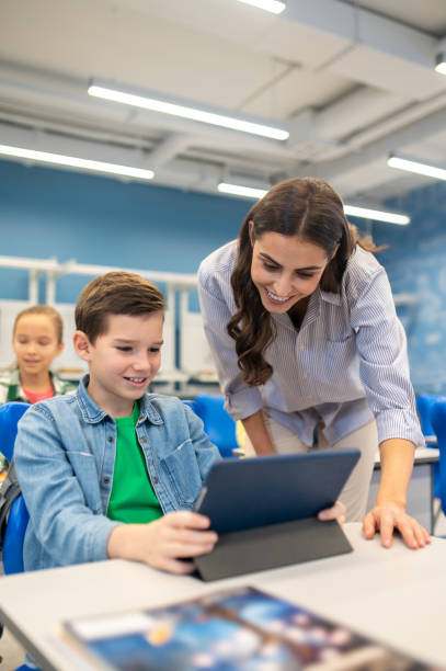 istock Teacher leaning over tablet of studying boy 1370537094