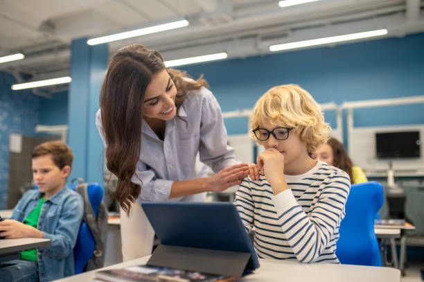 istock Smiling teacher touching shoulder of boy looking at tablet 1370537117