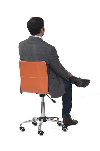 rear and side view of a man sitting on a chair wiith blazer and jeans legs crossed on white background