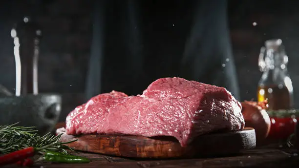 Raw beef steak placed on wooden cutting board. Preparation of meat, dark background.