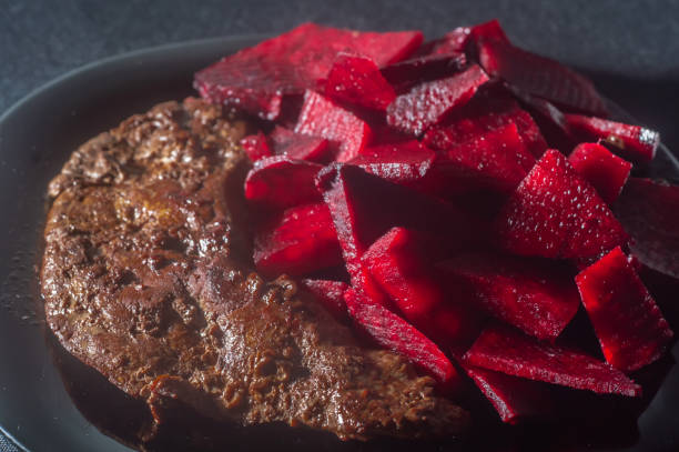 Fried ox liver with beetroot and placed on a black plate with onions, copy space on the left, Brazilian food.