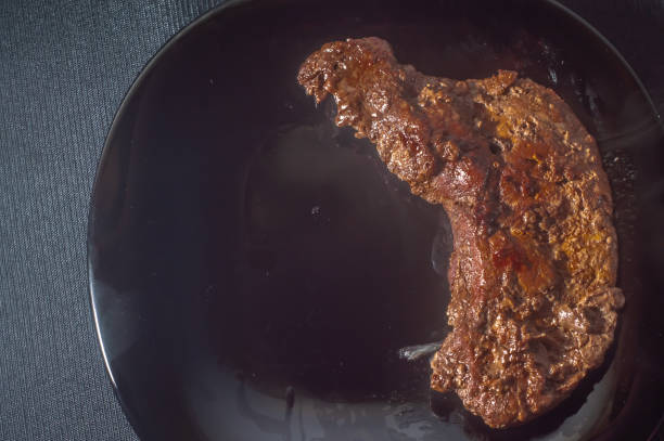 Fried ox liver, Brazilian food and placed on a black plate with onions, copy space on the left