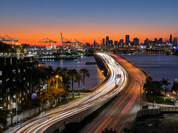 farbenfroher sonnenuntergang über miami downtown von miami beach aus gesehen, lange exposition des fließenden verkehrs über macarthur causeway, florida, usa. - south beach miami florida night florida stock-fotos und bilder